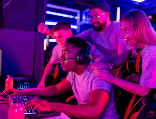Learn How To Make Money In The Gaming Industry A Gamer's Guide image 4 people stood in front of a screen with one with headset on all animated and smiling make xtra money online